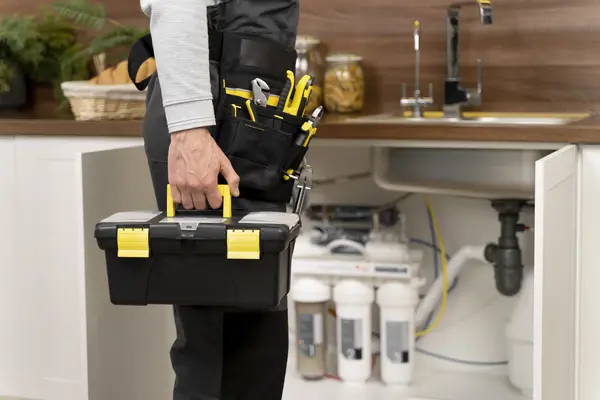 Plombier Lyon 8 : votre expert en dépannage rapide en 2025 ! 6 Plombier Lyon 8 portant une boîte à outils, prêt à réparer la plomberie sous un évier de cuisine